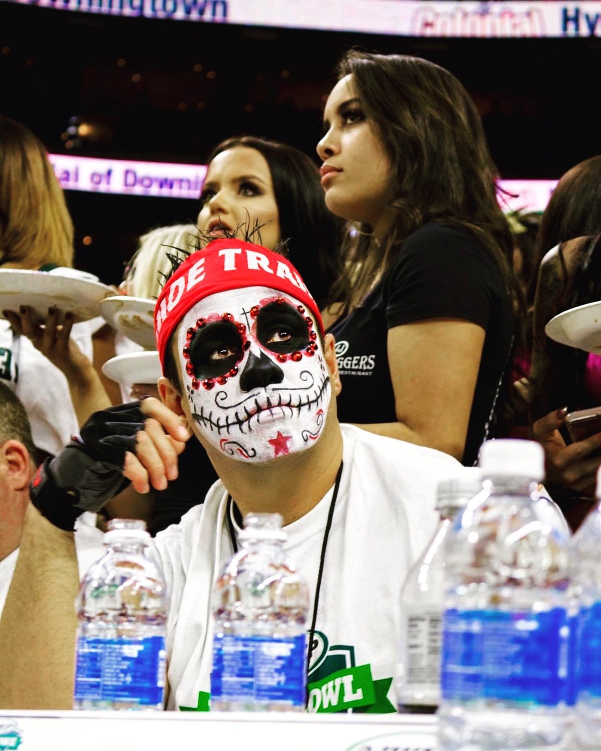 Moe in sugar skull paint at the Wing Bowl eating table as Wingettes serve plates