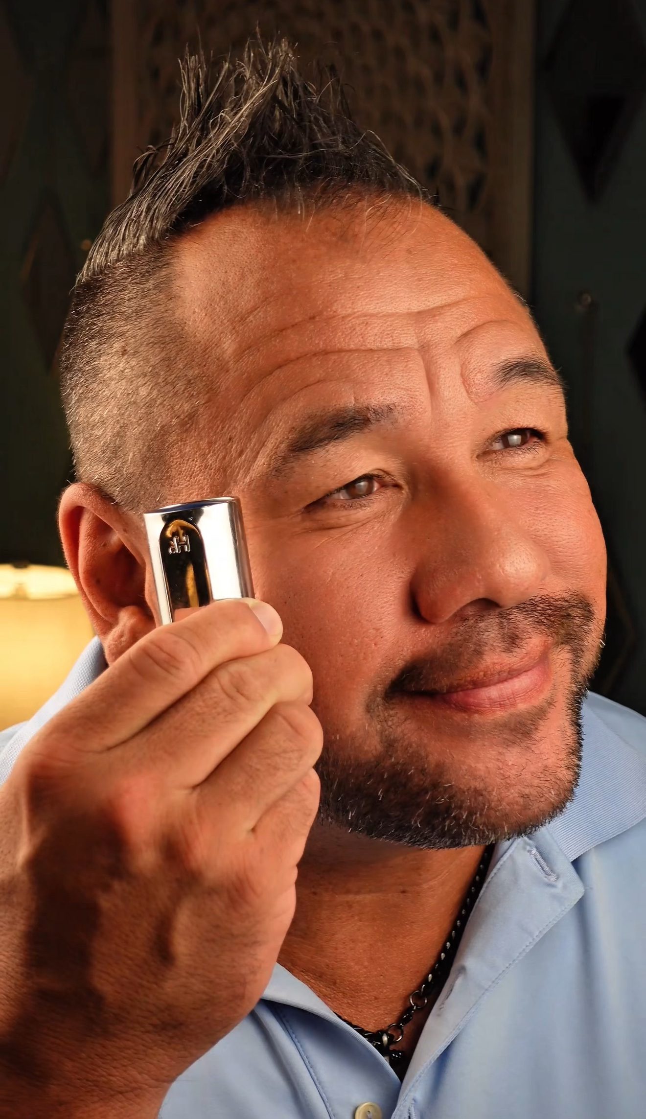 Close-up of Moe holding a chrome fragrance bottle beside his face
