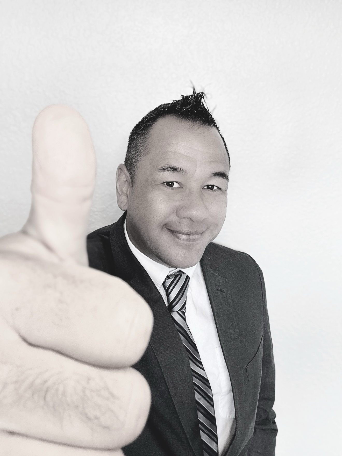 Black and white portrait of Moe in a suit giving a thumbs up to the camera